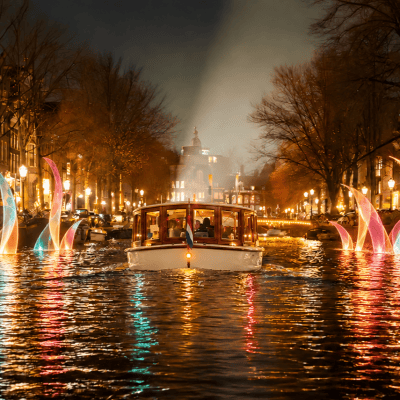 Illuminated boat on canal surrounded by colorful light installations at night.