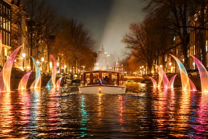 Illuminated boat on canal surrounded by colorful light installations at night.