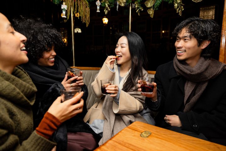 Friends smiling and drinking in a cozy setting with festive decorations.