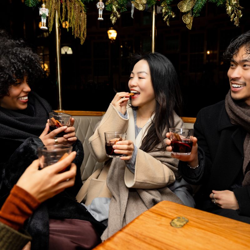 Friends smiling and drinking in a cozy setting with festive decorations.