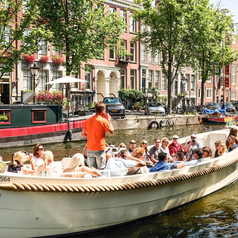 a small boat in a body of water with San Antonio River Walk in the background
