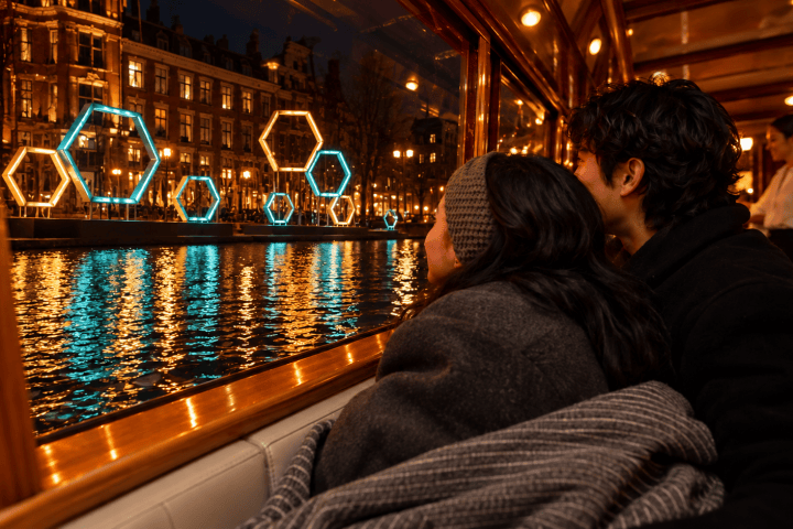 Couple on a boat enjoy nighttime city lights reflecting on water.