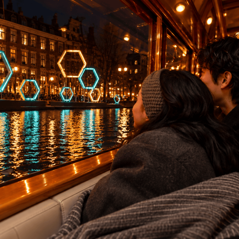 Couple on a boat enjoy nighttime city lights reflecting on water.