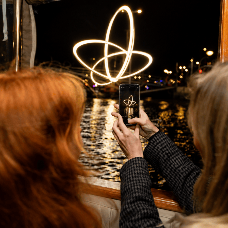 Two people photograph light trails on a boat at night.